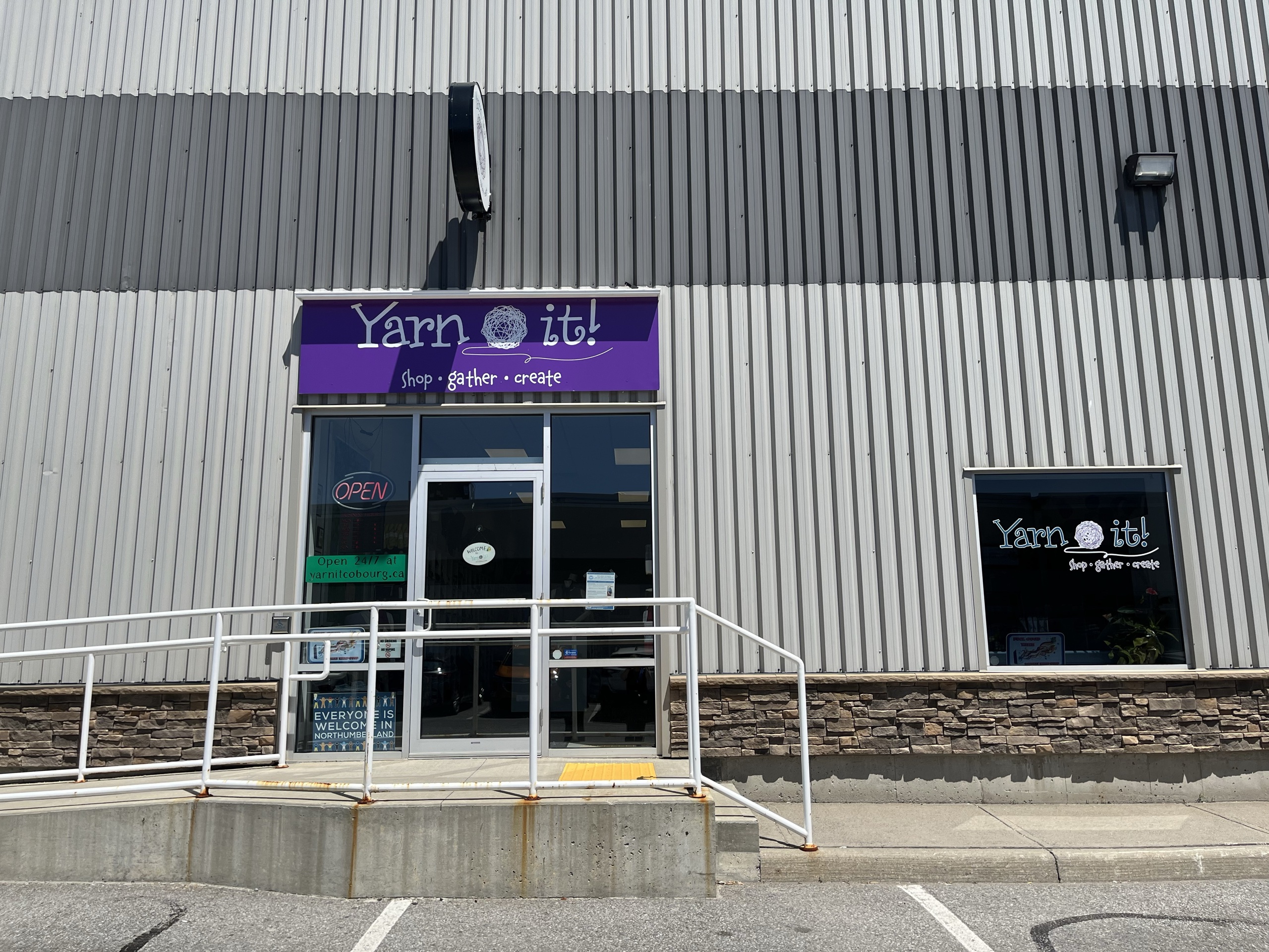 Photo capturing storefront. Grey exterior with a purple sign above the door reading "Yarn It".