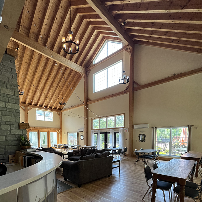 High ceiling room with tables, chairs and couches with lots of natural lighting and string lights.
