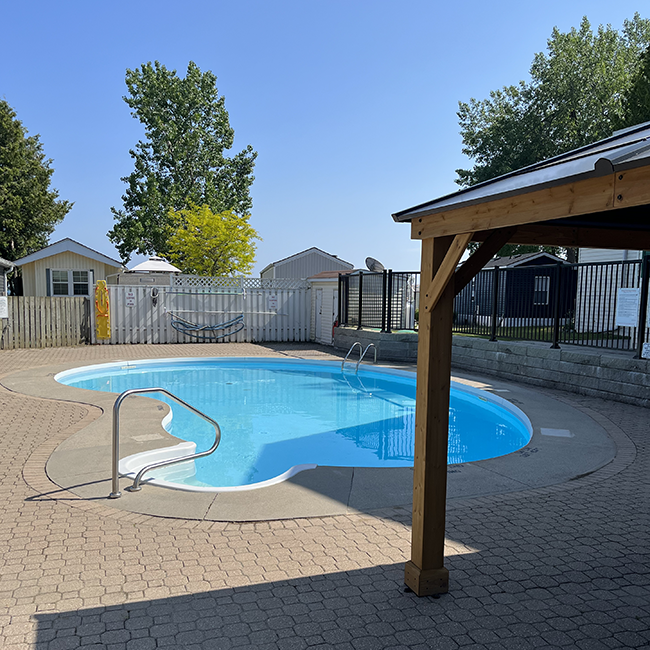 Oval shaped inground pool with cabana surrounded by a fence.