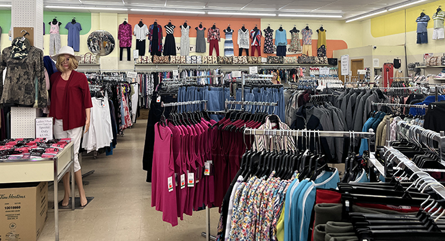 Racks of women's clothing items with mannequins hanging on the wall displaying clothing.