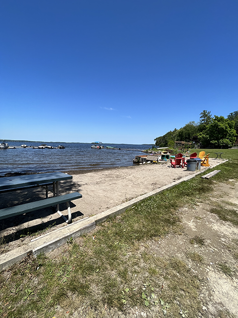 Small beach with a picnic table and adirondack chairs overlooking lake.