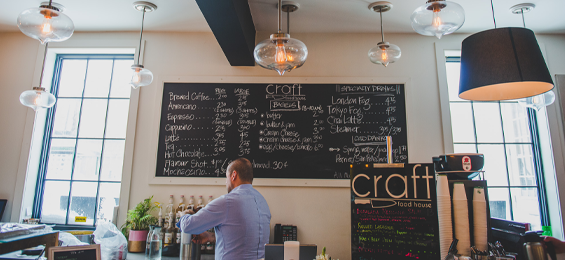 man standoing in a large bright room in front of a large chalkboard menu.