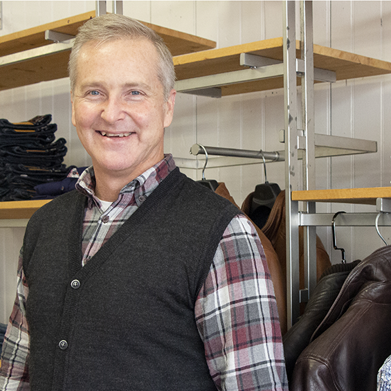 Man smiling in front of clothing racks.
