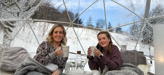 2 women drinking hot chocolate under a blanket.