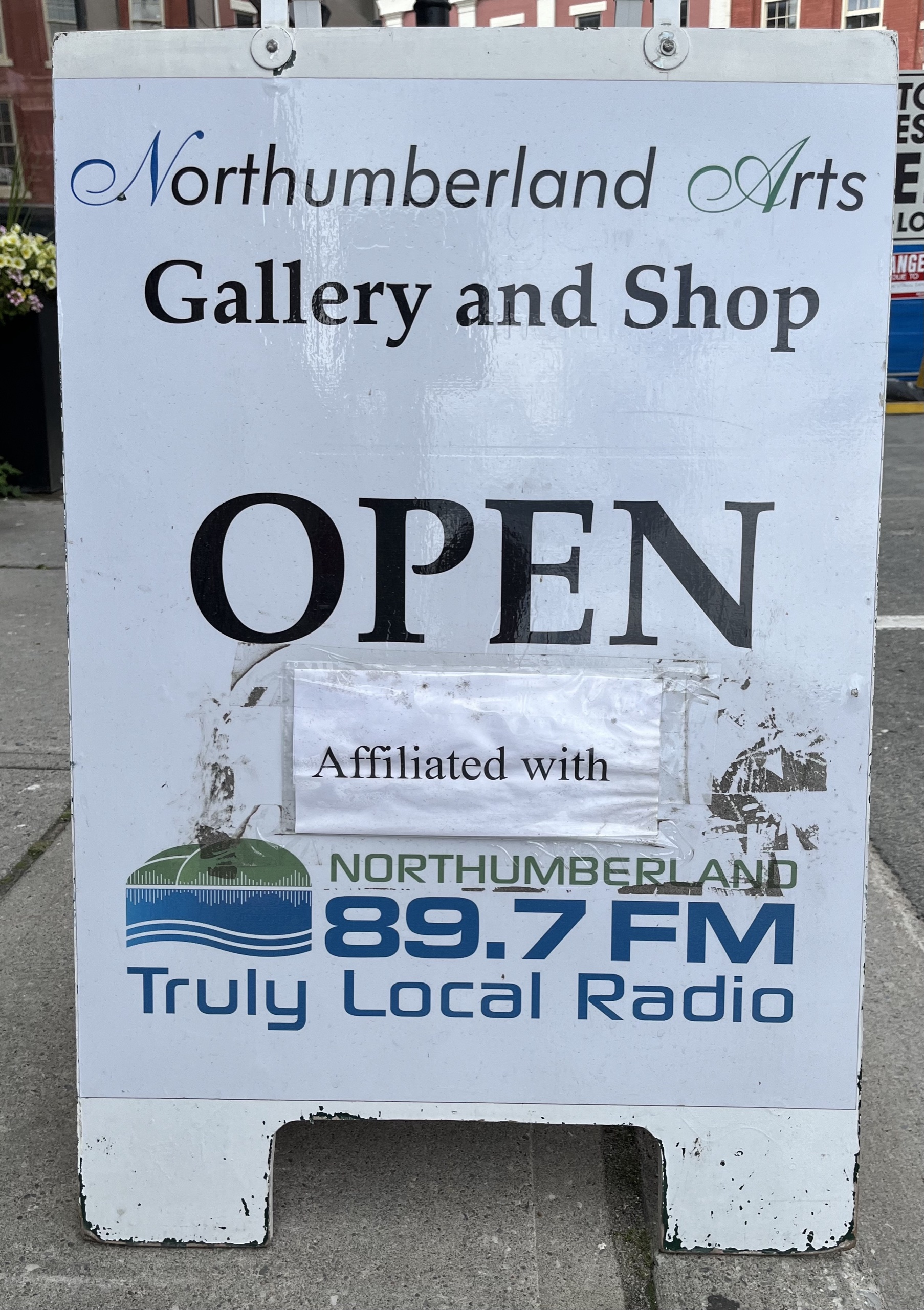 Photo of sign outside of Northumberland Arts Gallery and Shop. Sign reads "Northumberland Arts Gallery and Shop. Open. Affiliated with Northumberland 89.7 FM Truly Local Radio."
