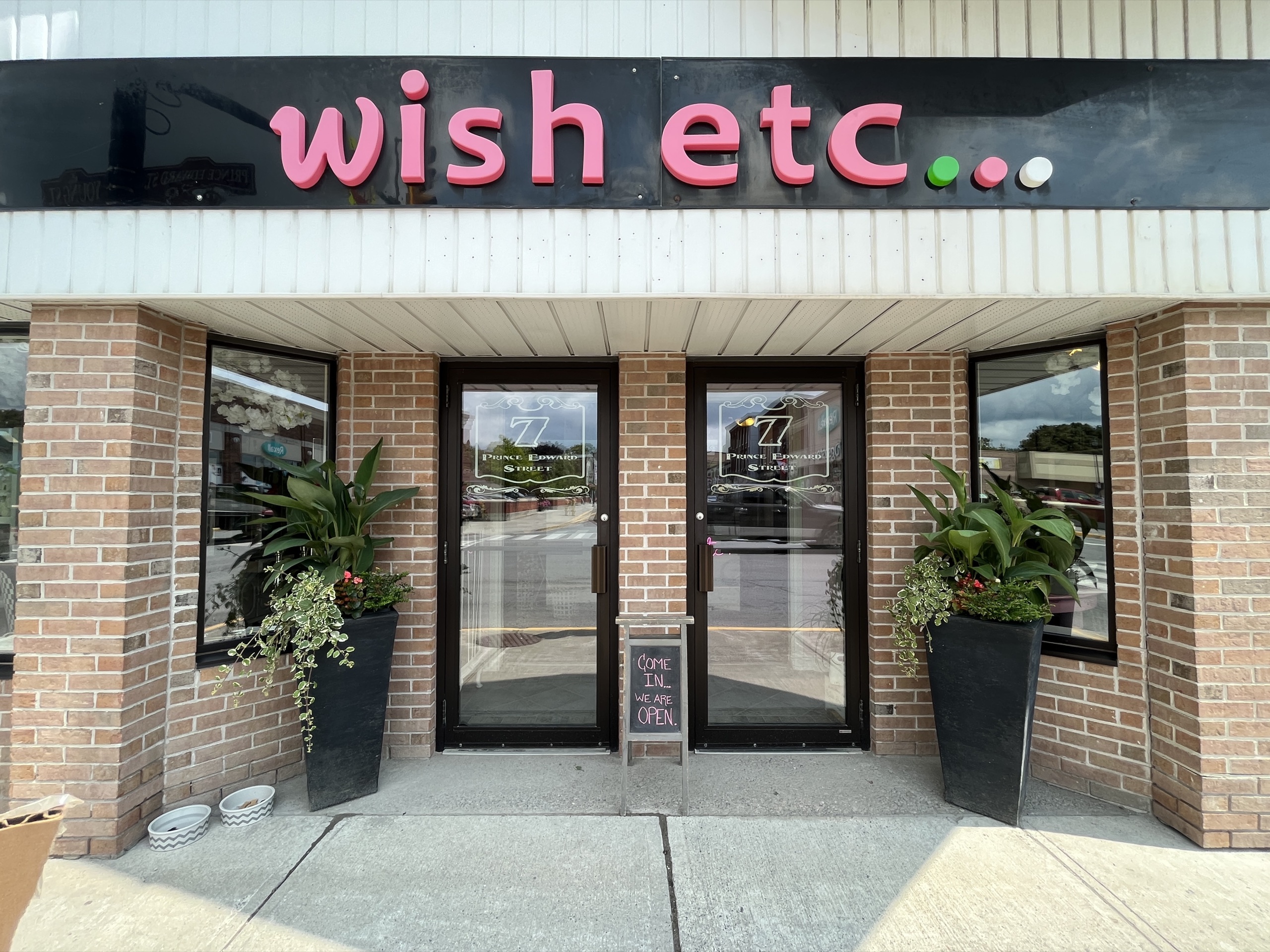 Photo of storefront. Sign above the doors reads "Wish Etc..." in pink.