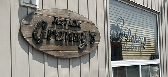 Wooden sign with black wood lettering on a grey building.