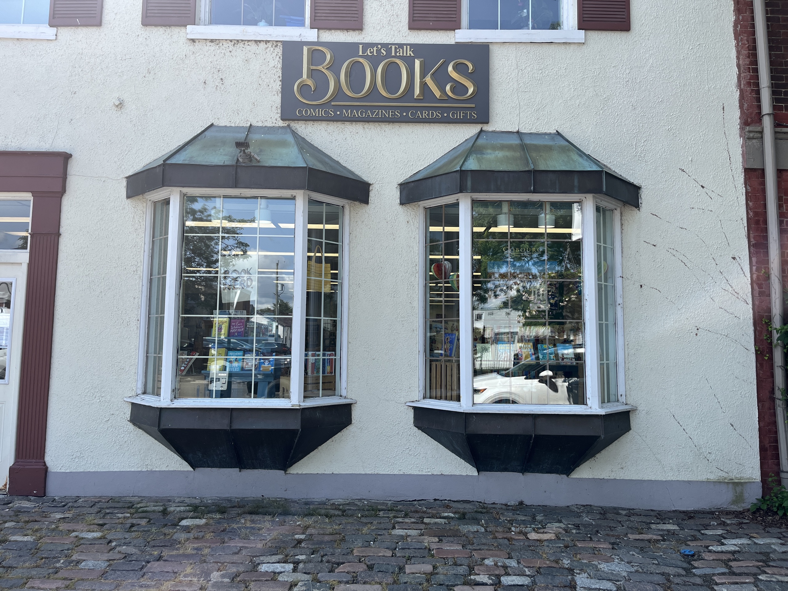 Photo of Readers Nook store front. Photo features a sign above two windows reading "Let's Talk Books."