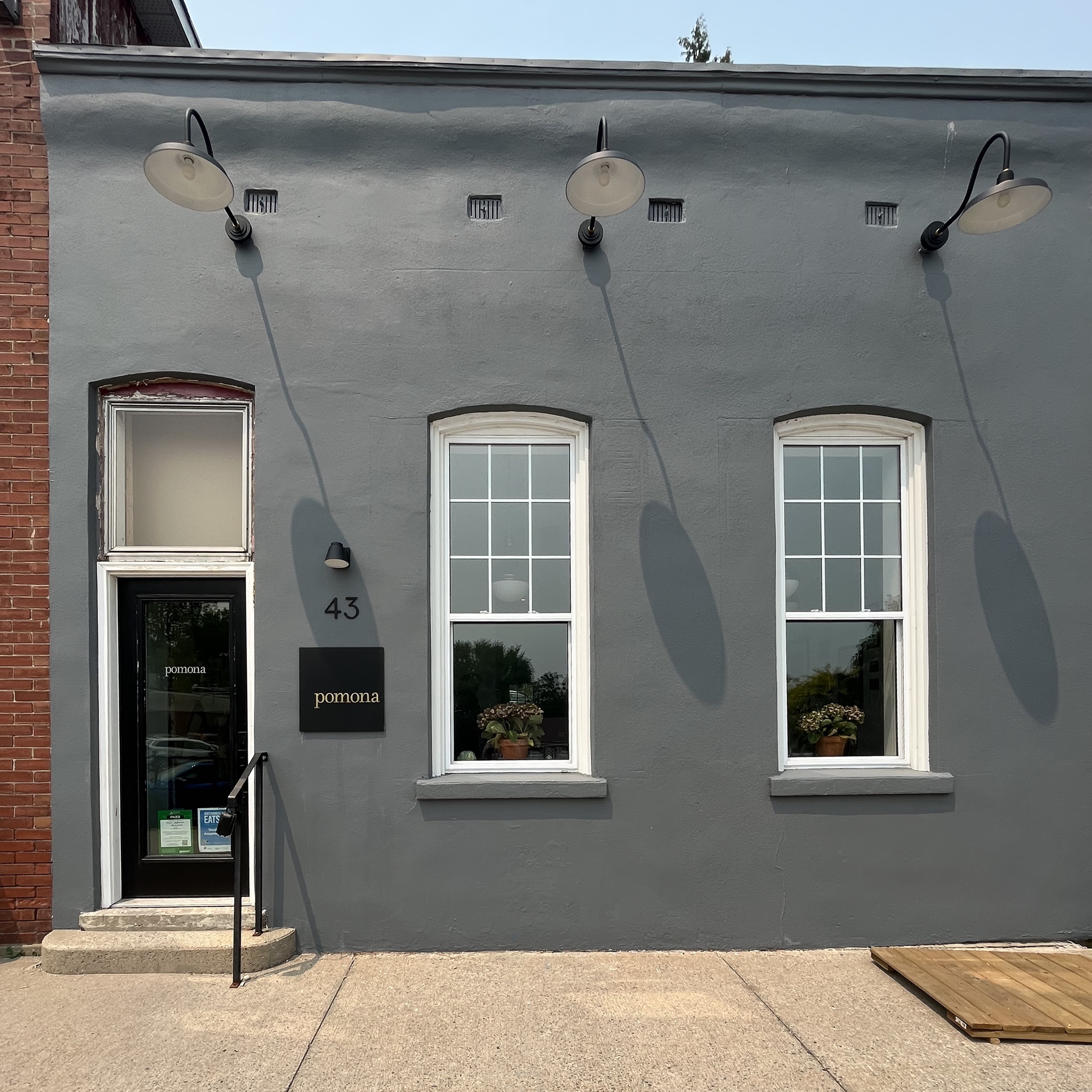 Grey building with 3 large spotlights over 2 windows and a door with small black sign.