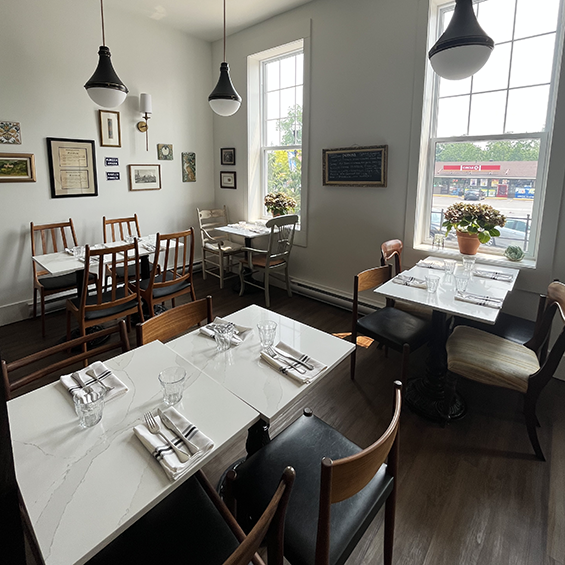 4 tables set for eating in a restaurant with white walls and drop lights.