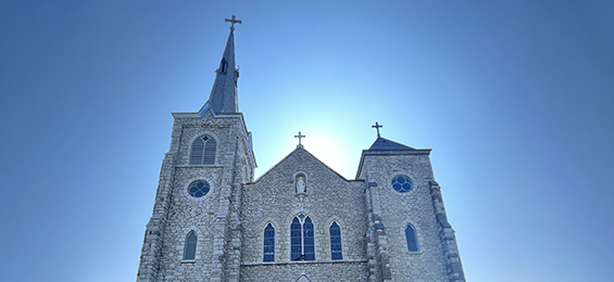 Large stone building with stained glass windows and 3 crosses on the top.