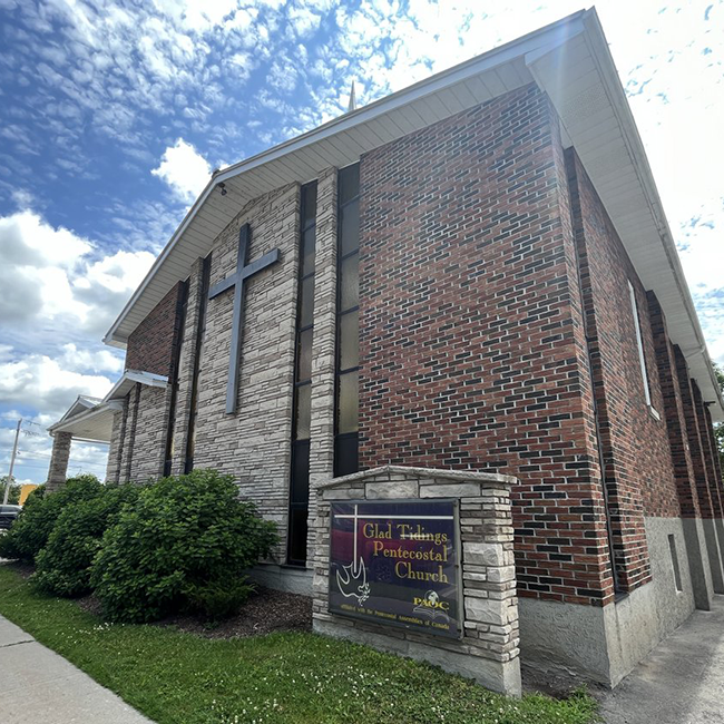 Large brick building with a large black cross on the front with bushes in front.