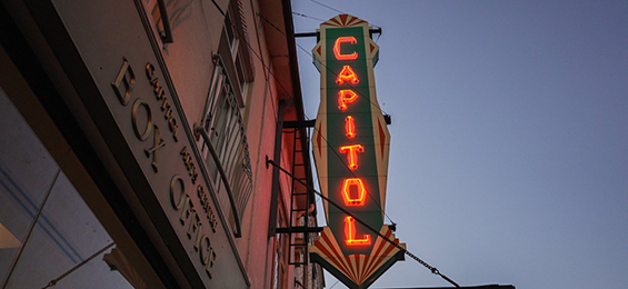Vertical green sign with red LED writing on the side of a building.