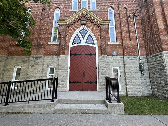 Grey and red brick building with large red doors with white crowning and stained glass