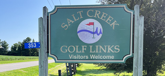 Green sign with yellow writing and a golf ball logo in the middle.
