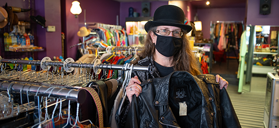 Person holding a leather jacket in a store full of clothes.