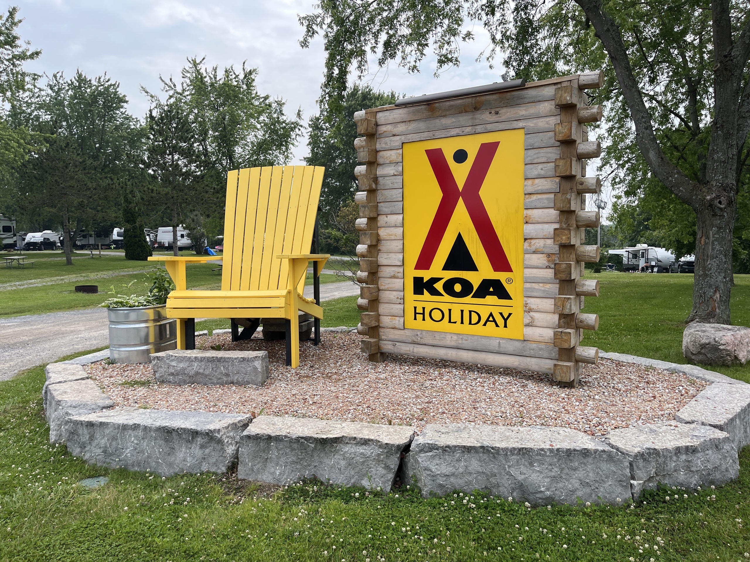 Photo of a giant chair beside the KOA sign. The sign reads "KOA Holiday" with the KOA Brighton logo above the text.