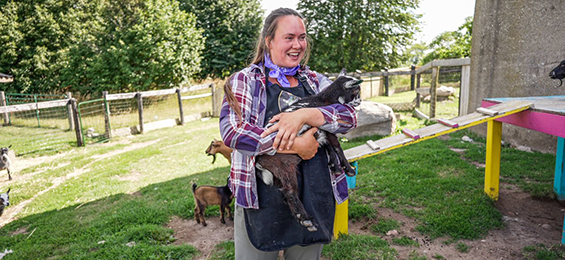 Woman smiling holding a goat in a pen full of goats.