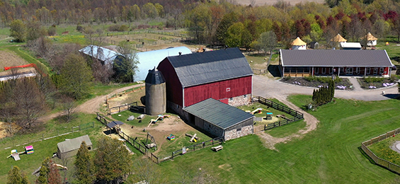 Red barn with a fenced in barnyard beside a house.