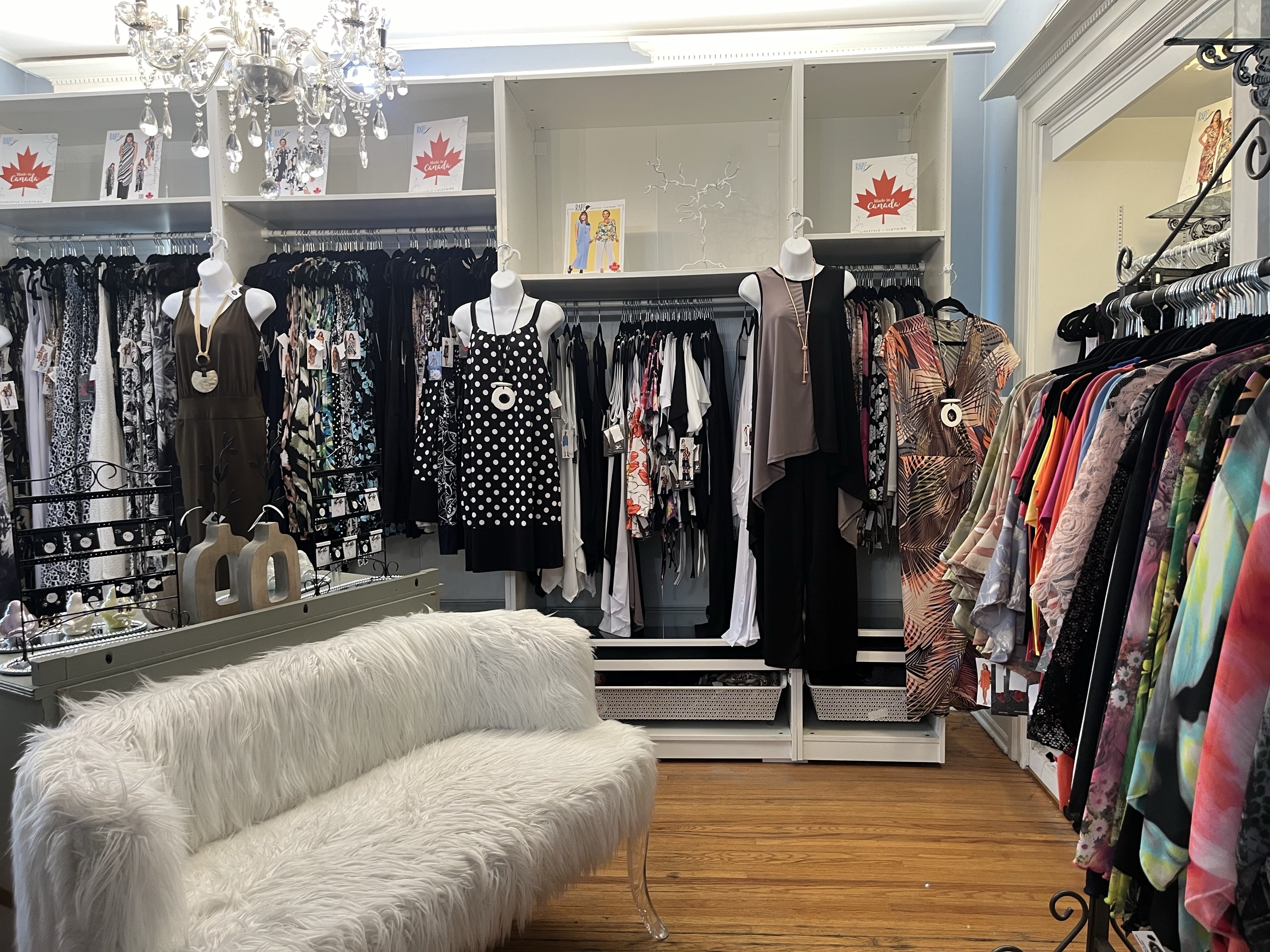 Photo of inside the store. Womens clothes hung up and covering the entire wall. Small fabric bench in the middle.