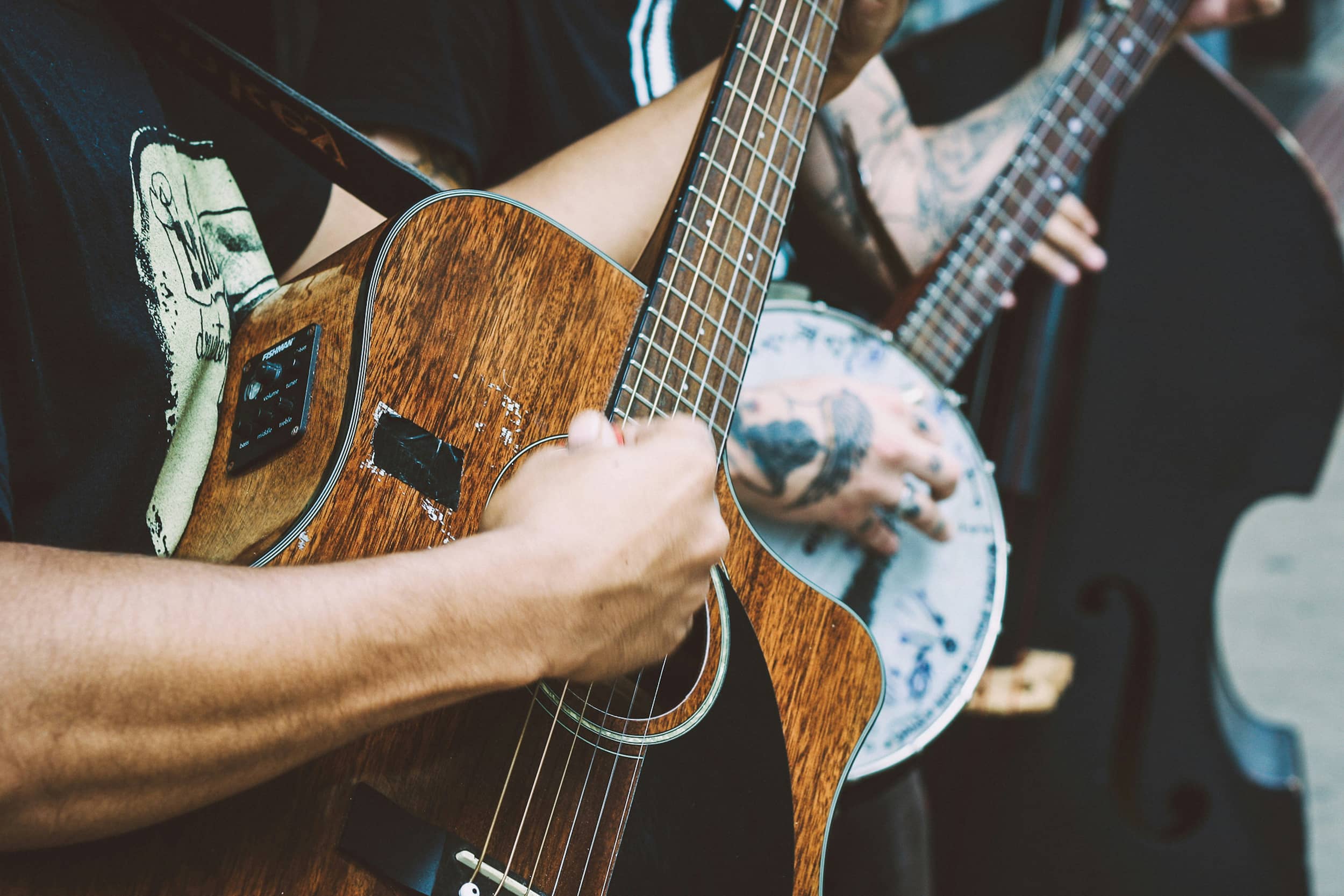 Detail of a person playing a guitar and another person playing banjo in the background.