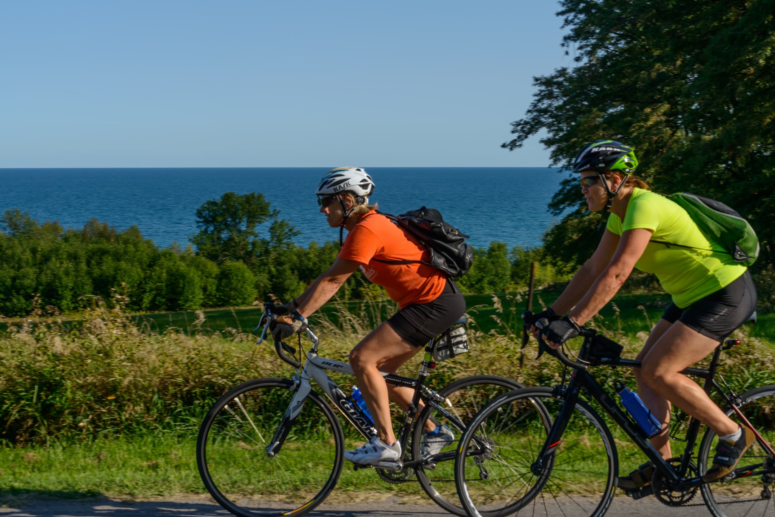 Two women riding bikes along the water
