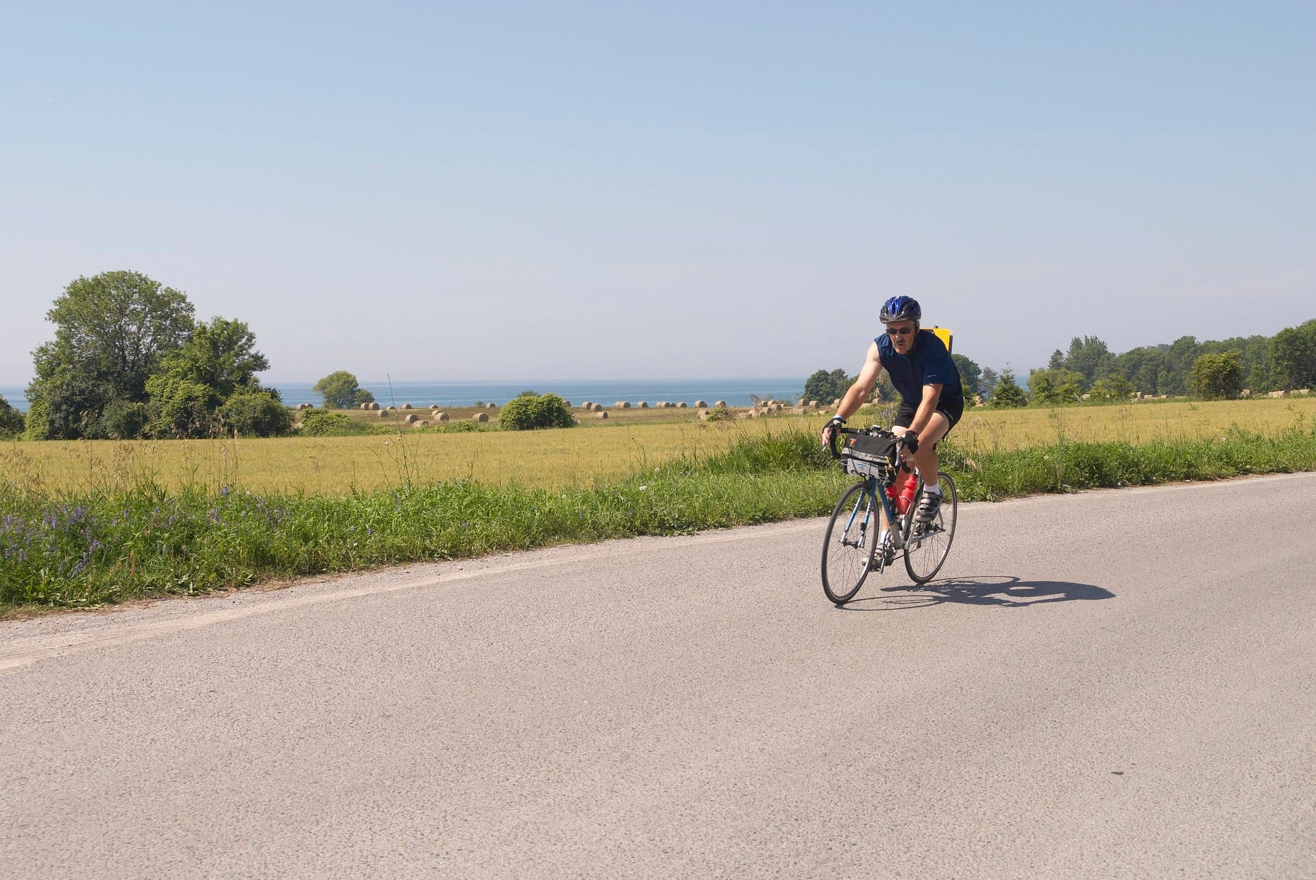 Man riding a bike along a country road by Lake Ontario