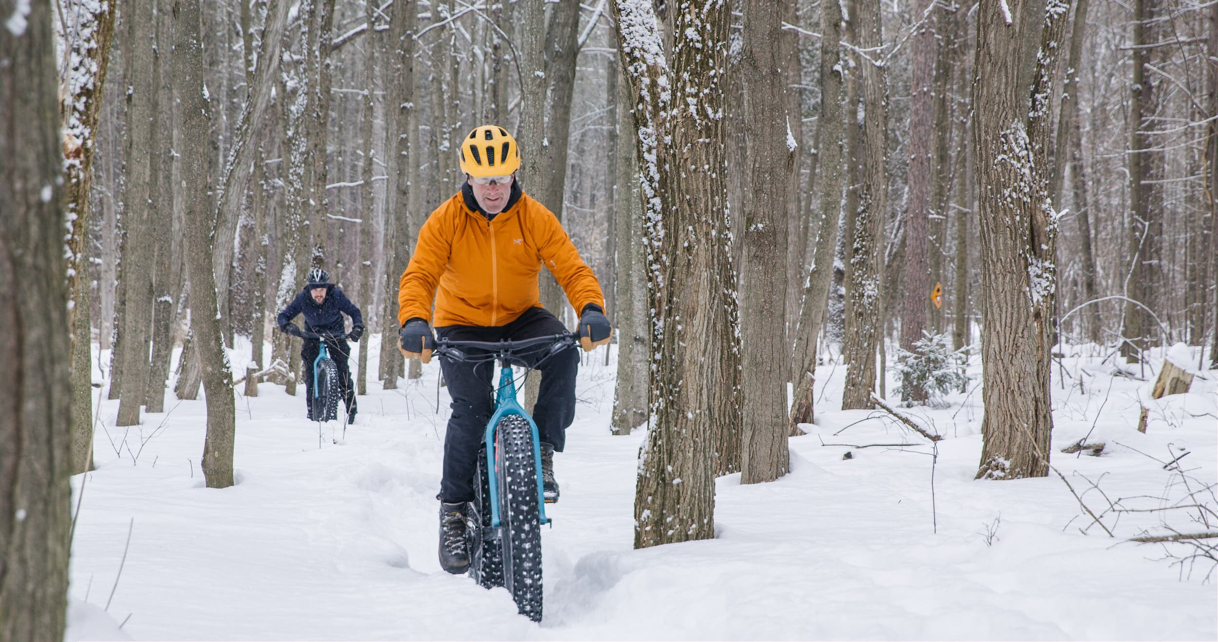 Man in an orange coat rides a fat bike in the forest in winter