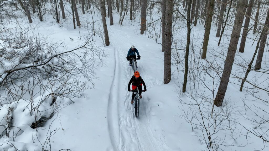 Drone view of two people fat biking in a snow covered forest