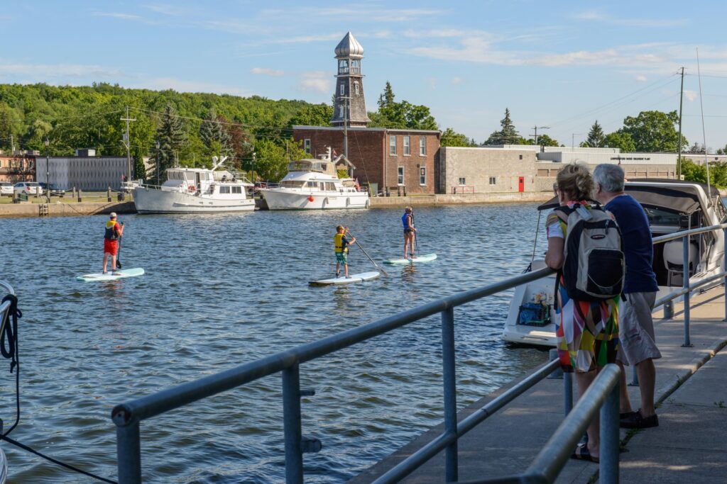paddle boarders on river with people watching from the shore