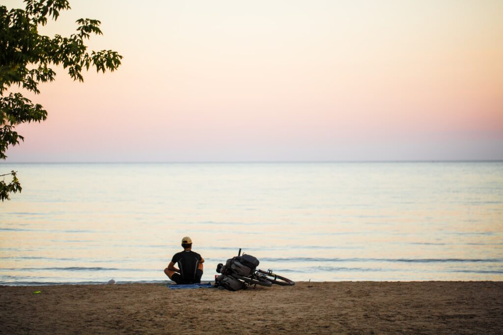 Man sitting at the edge of Lake Ontario at Port Hope Beach with his bike beside him