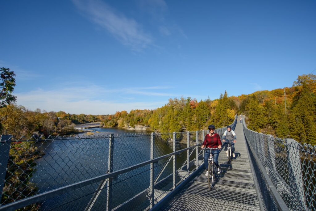 Two people riding bikes over a large suspension bridge