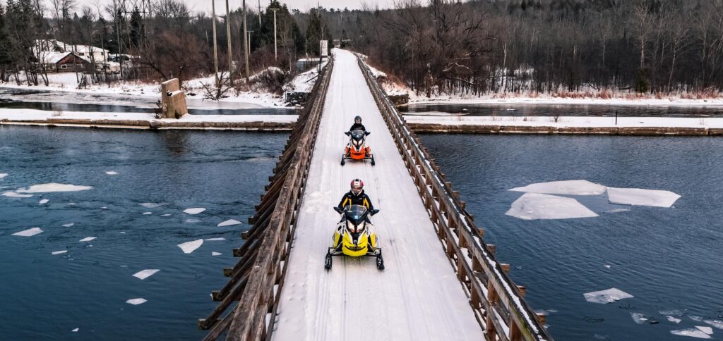 two motorcycles driving across a snowy bridge over icy water