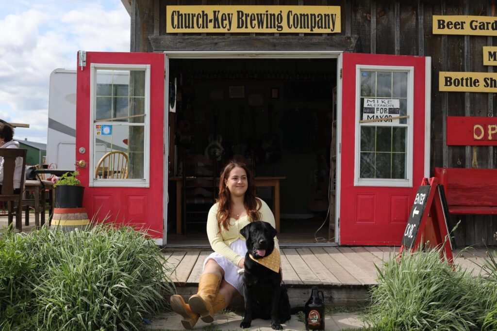 Woman with a black lab sitting in front of Church Key Brewing Company