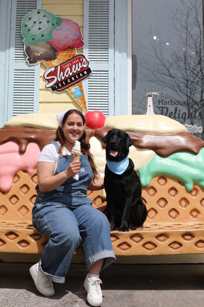Woman sitting on a bench decorated as a waffle cone while holding an ice cream cone design her black lab