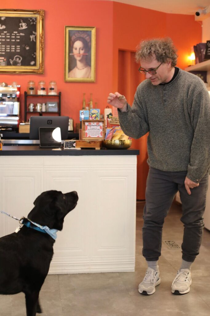 Male shop owner giving a treat to a black lab