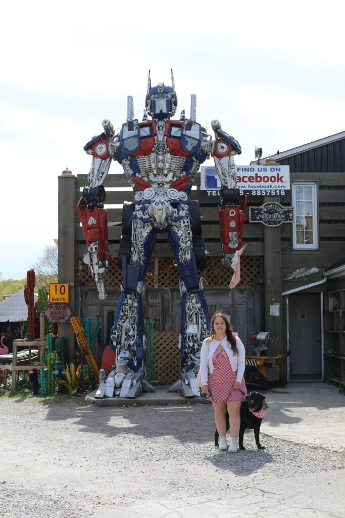 woman and her dog walking in front of a large robot sculpture
