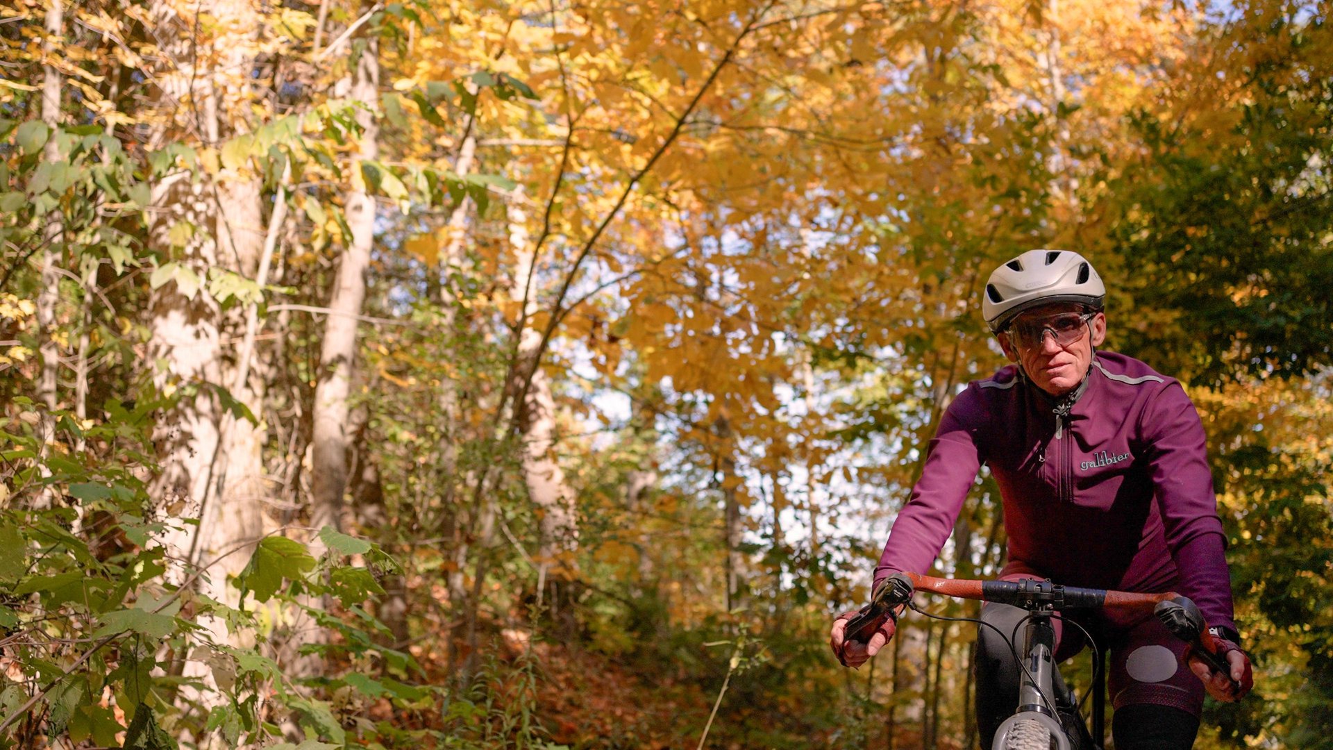 Man cycling by trees covered in fall colours