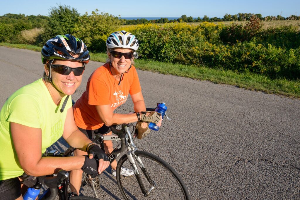 Two female cyclists smiling at the camera with their bikes and wearing helmets