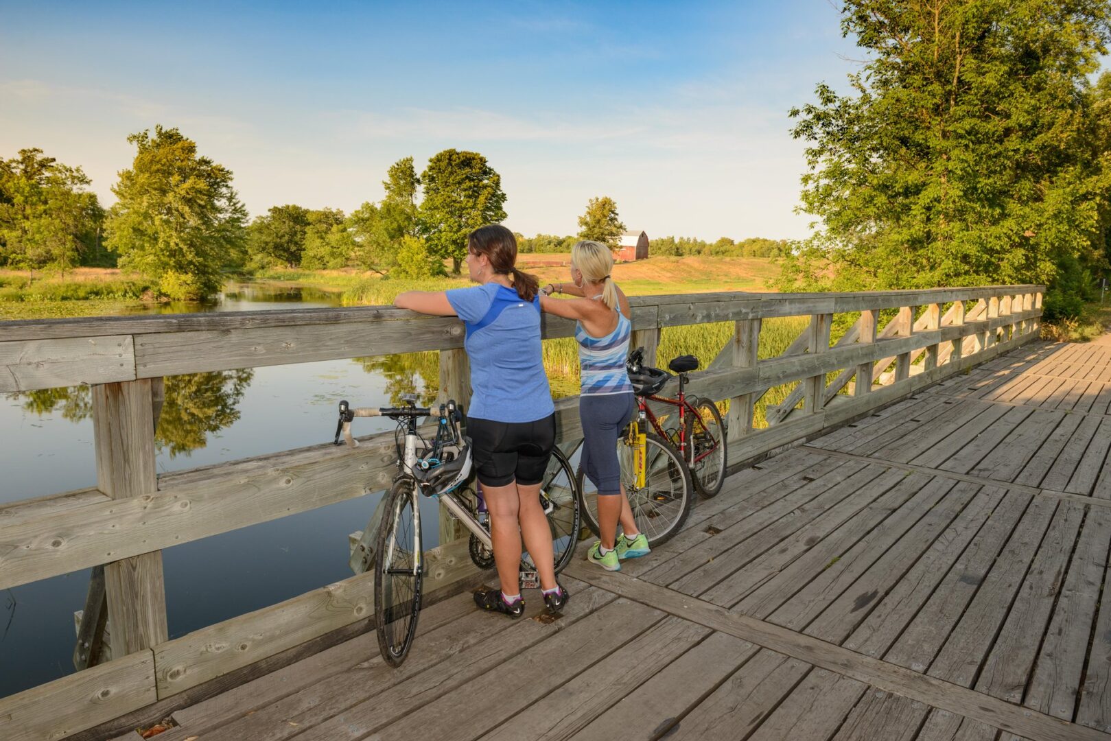 Two women standing by bikes looking over a bridge railing at a pond