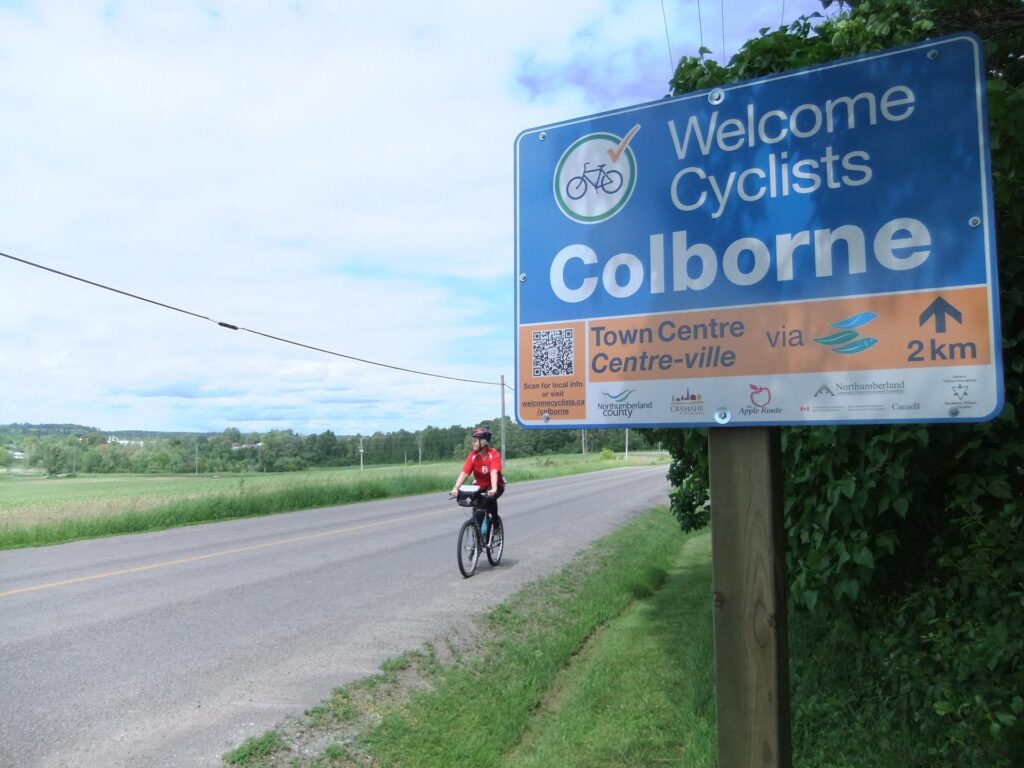 Cyclists Welcome in Colborne sign with a cyclist riding towards it