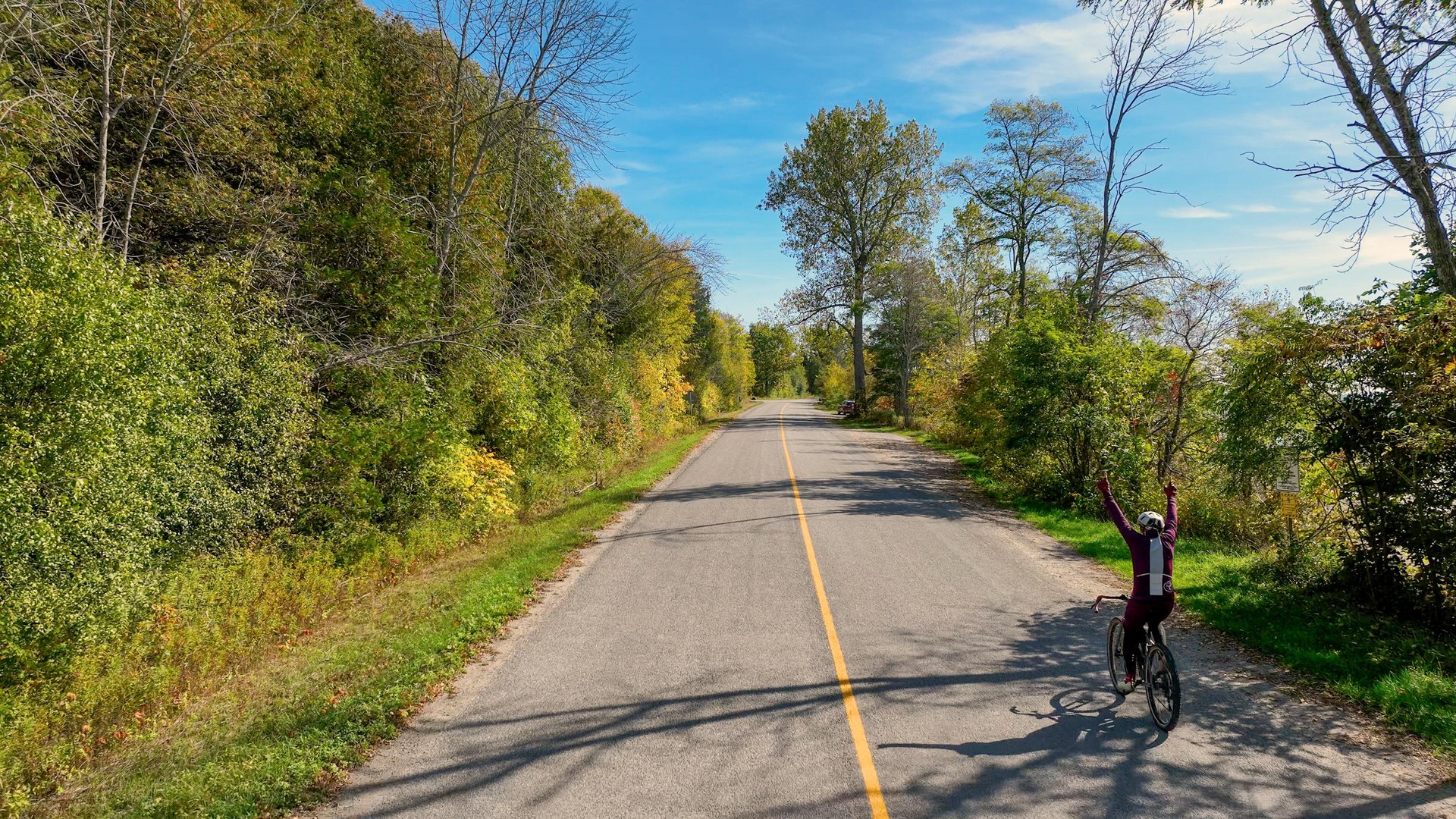 Man with his arms in the air riding along a country road