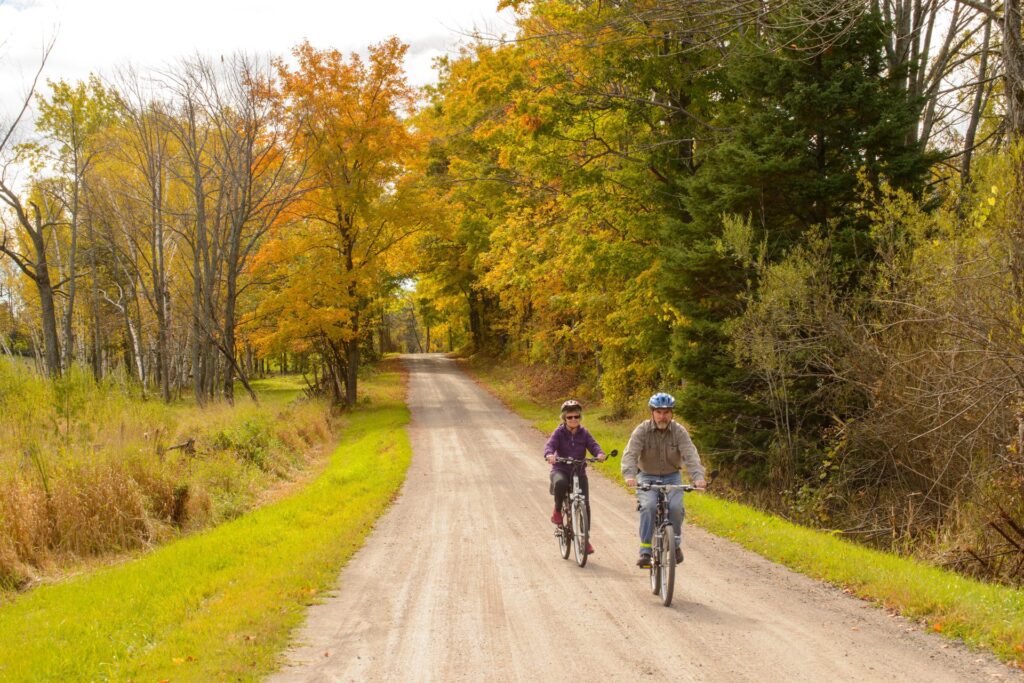 Two people riding bikes on a dirt road with fall colours surrounding them