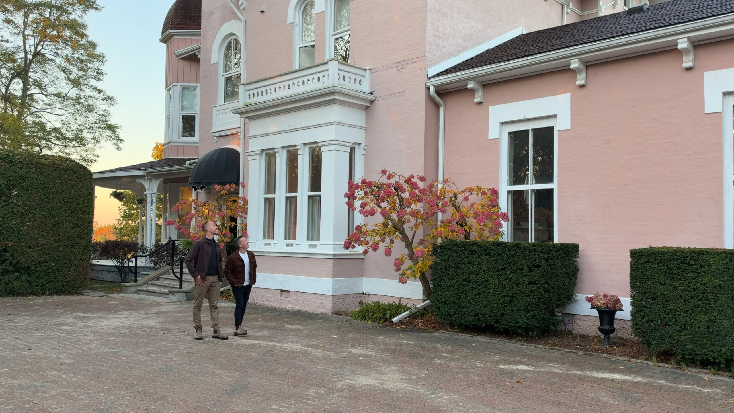 2 men walking outside a pink Italianate style bed and breakfast.