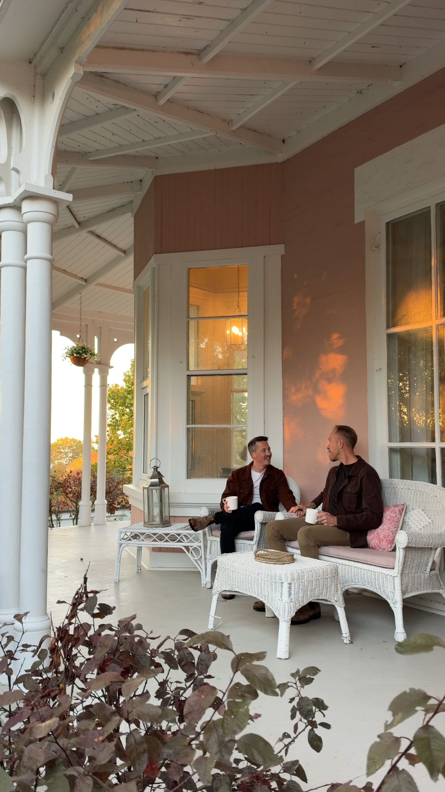 2 men sitting on a porch of a pink Italianate style bed and breakfast.